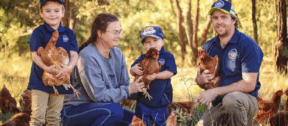 The Watson family of Watson Family Produce, with their children, standing on their farm holding chickens.