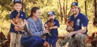 The Watson family of Watson Family Produce, with their children, standing on their farm holding chickens.