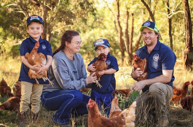 The Watson family of Watson Family Produce, with their children, standing on their farm holding chickens.