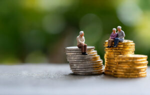 Miniature elderly figures sitting on coin stacks, symbolising retirement savings and financial security.