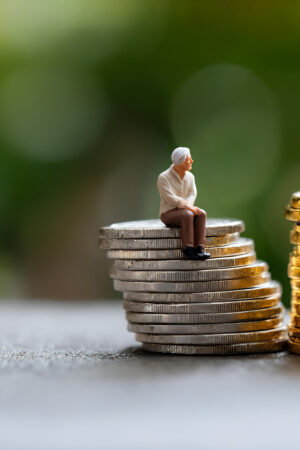 Miniature elderly figures sitting on coin stacks, symbolising retirement savings and financial security.