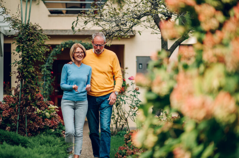 Retired couple walking in front yard of home
