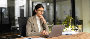 A business owner reviewing financial figures on a laptop at a bright, uncluttered desk, considering their tax position for the year ahead.