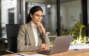 A business owner reviewing financial figures on a laptop at a bright, uncluttered desk, considering their tax position for the year ahead.
