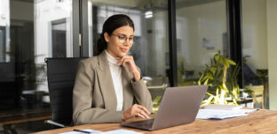 A business owner reviewing financial figures on a laptop at a bright, uncluttered desk, considering their tax position for the year ahead.