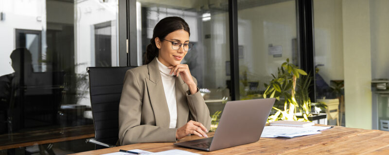 A business owner reviewing financial figures on a laptop at a bright, uncluttered desk, considering their tax position for the year ahead.