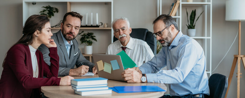 A multi-generational family group reviewing documents and notes on a laptop as they discuss proposed changes to discretionary trust taxation in Australia.