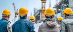 People wearing hard hats review project plans at a large industrial construction site. The image reflects infrastructure development and business planning associated with major defence-related projects and supply chain opportunities in the Northern Territory.