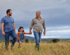 Three generations of a farming family walking together through a paddock with cattle grazing behind them, showing the long term planning a family advisory board supports.