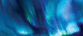 Aurora lights sweeping across a dark night sky in vivid blue, teal and green, with scattered stars visible through the glow.