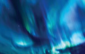Aurora lights sweeping across a dark night sky in vivid blue, teal and green, with scattered stars visible through the glow.