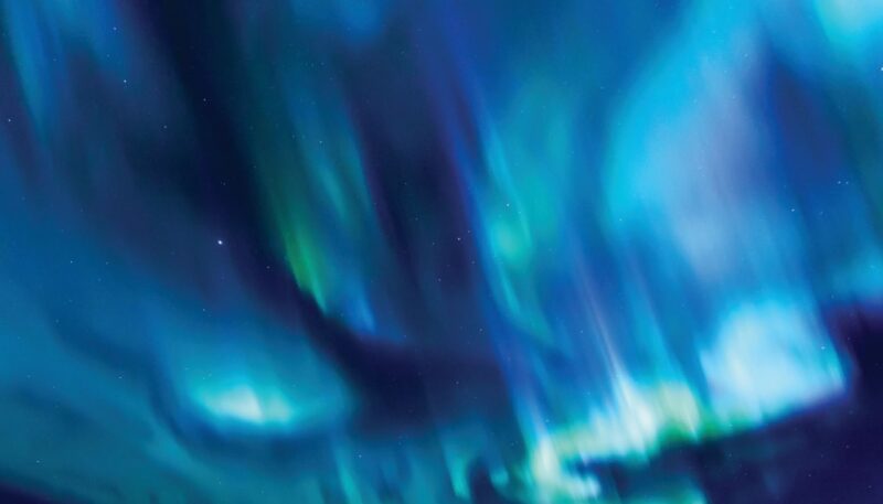 Aurora lights sweeping across a dark night sky in vivid blue, teal and green, with scattered stars visible through the glow.